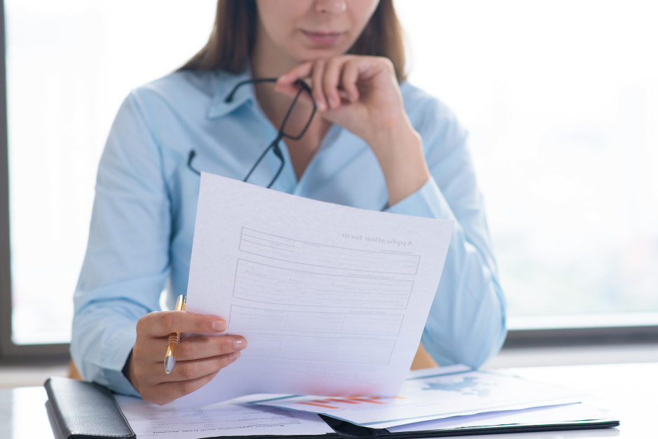 A woman holding a printed report and glasses at a desk, illustrating review of medical records before travel