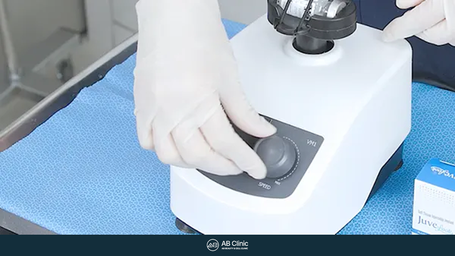 手袋を着けた手が白い混合機器の操作部分に触れている接写。右端にジュベルックの箱の一部が写る。